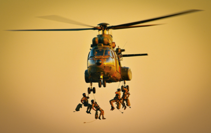 A military helicopter with members of the military repelling out of it.