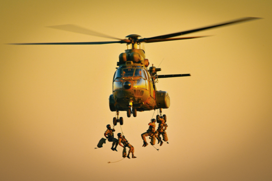 A military helicopter with members of the military repelling out of it.